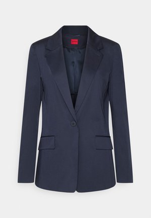 Donkerblauwe blazer met één knoop, notch-revers, twee voorzakken met klep en een rood Hugo-label aan de binnenkant van de kraag.