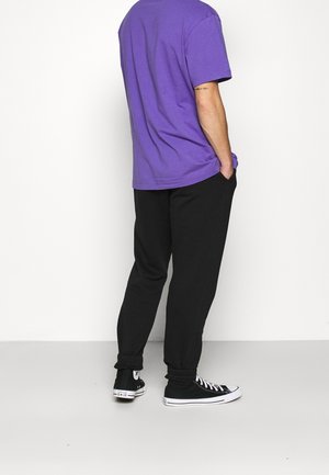 Fialové bavlněné tričko, volný střih, v kombinaci s černými jogger kalhotami. Černé tenisky s bílými podrážkami. Jednoduchý, neformální outfit.