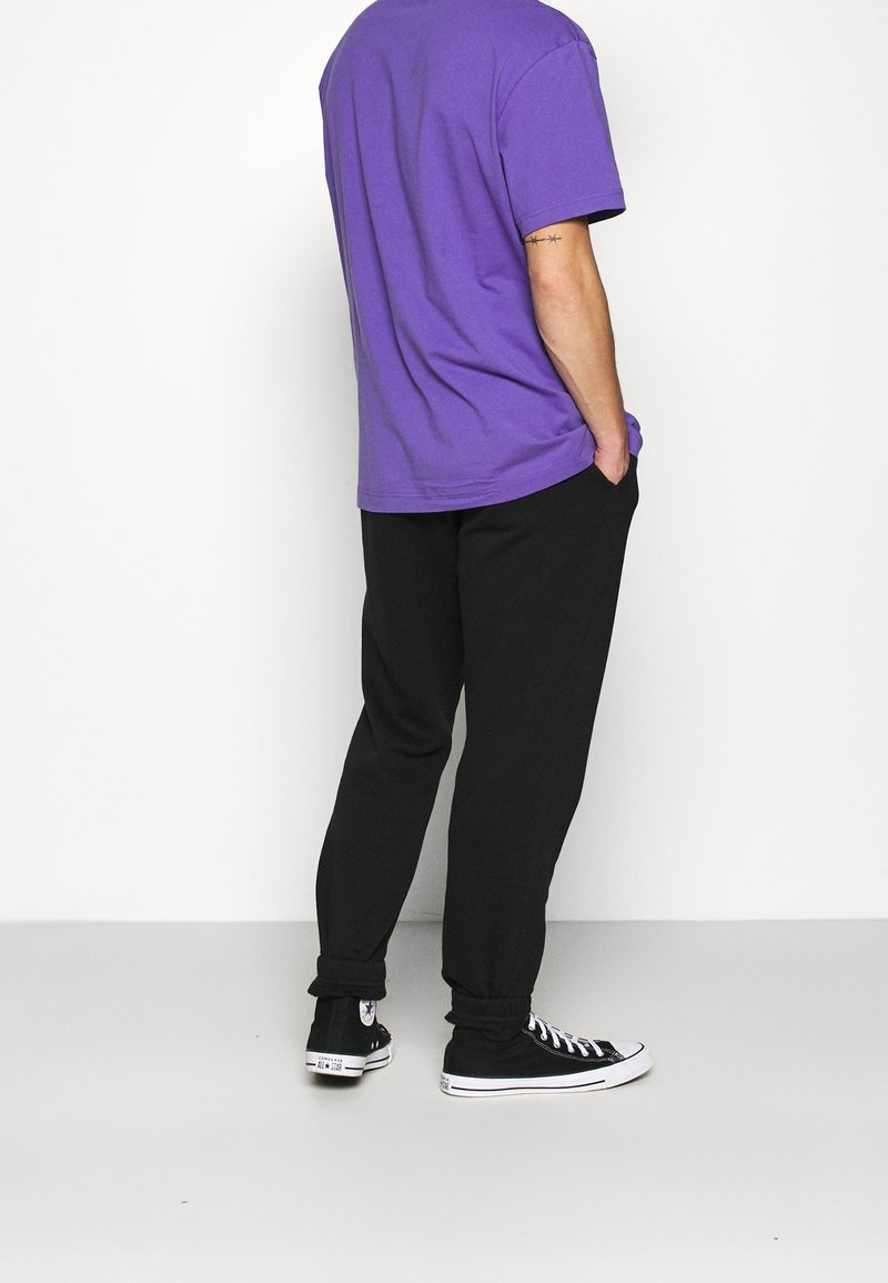 Fialové bavlněné tričko, volný střih, v kombinaci s černými jogger kalhotami. Černé tenisky s bílými podrážkami. Jednoduchý, neformální outfit.