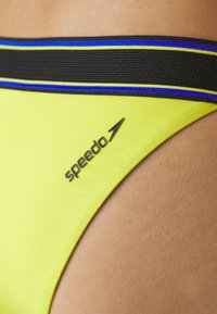 Gule svømmebokser med en svart elastisk midjebånd med blå og gule detaljer. "Speedo"-logoen vises i svart.