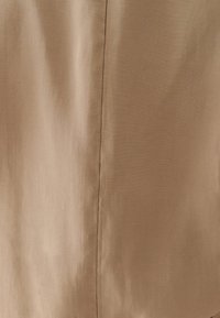 Tissu marron clair avec une texture lisse, présentant une couture verticale et un léger éclat. Le matériau semble léger et finement tissé.