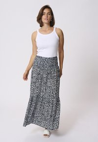 Jupe maxi à motifs bleu marine et blanc, en tissu léger avec une taille froncée, assortie d'un débardeur blanc uni et de sandales légères.
