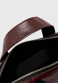 Vinrød læderhåndtaske med lynlås, topstykke og sort for med præget logoindlæg indvendigt. Metal lynlåshardware synlig.