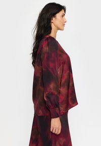 Maroon og brun gradient-bluse med lange ermer, mykt stoff og rynkede mansjetter. Designet med en løs passform for komfortabel bruk.