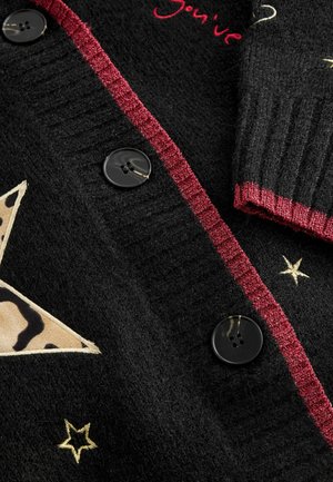 Black knitted cardigan with a red textured trim, featuring a large tan star with a leopard print, gold star accents, and black buttons.