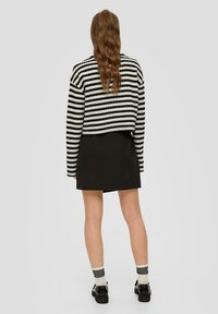 Zwart-wit gestreepte trui met een cropped ontwerp, gecombineerd met een zwarte rok. De schoenen zijn zwarte platform schoenen en de sokken zijn gestreept.