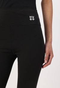 Zwarte leggings met een getailleerd ontwerp, gemaakt van zachte stof, met een brede tailleband en een geborduurd "HUGO" logo aan de voorkant.