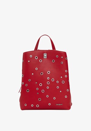 Raudona odinė kuprinė su sidabro žiedais, stačiakampio formos, su viršutiniu rankena ir užtrauktuku. Apatinėje dalyje yra logotipo detalė.