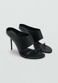 Mules nere con tacco alto e finitura in pelle lucida. Presentano una fascia superiore ampia e un sottile cinturino sulla punta. Design elegante e minimalista.