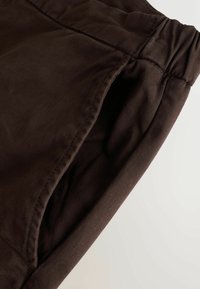 Braune Stoffshorts mit elastischem Bund, die über eine glatte Textur und diagonale Nahtdetails an der Seite verfügen.