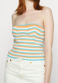 Top sin tirantes de canalé con rayas horizontales en naranja, blanco y turquesa, combinado con una falda de mezclilla blanca de cintura alta.