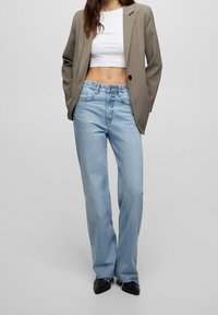 Jean bleu clair taille haute avec une coupe droite, associé à un crop top blanc et un blazer beige. Chaussures noires à bouts pointus.