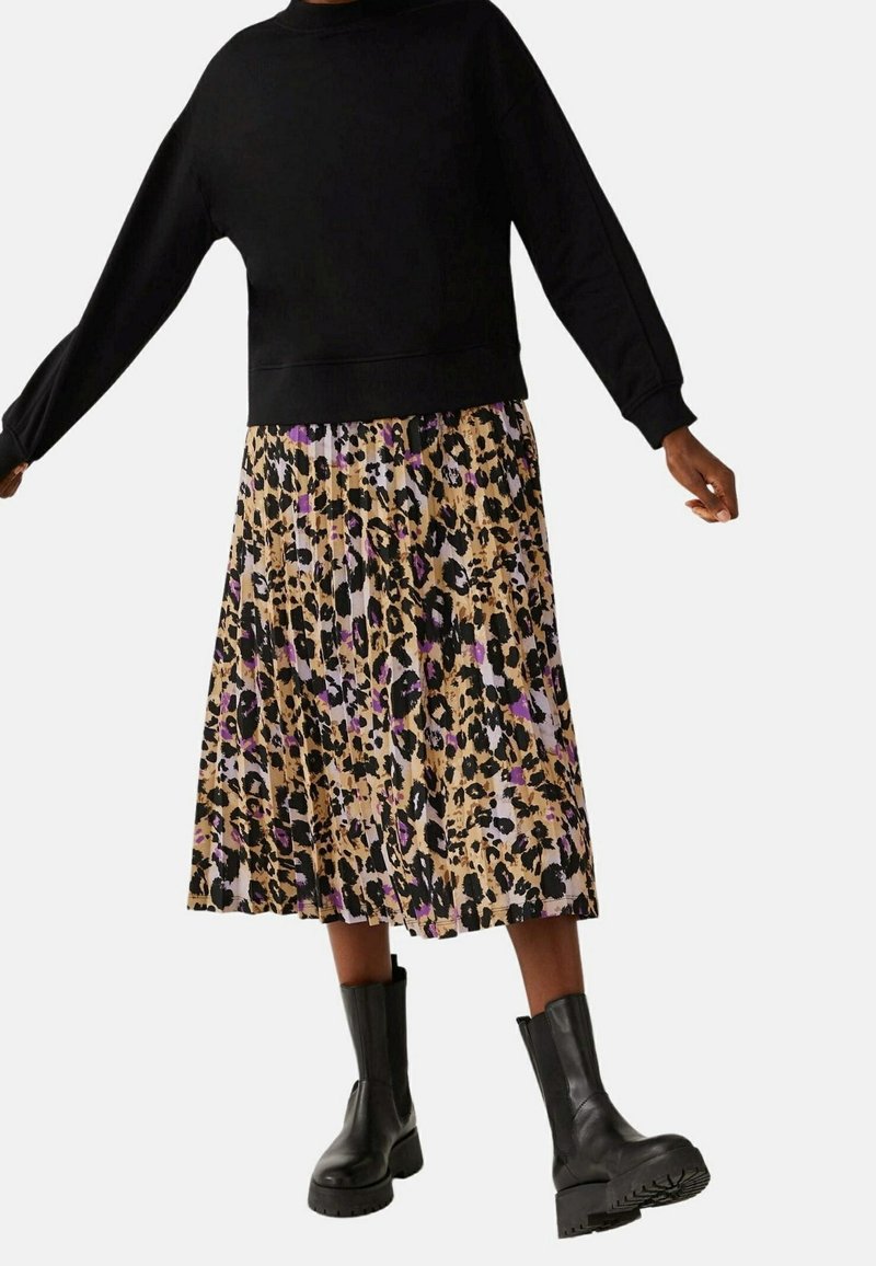Zwarte sweatshirt met lange mouwen, gecombineerd met een geplooide rok met een luipaardprint in beige, paars en zwart. Zwarte chunky-heeled laarzen.