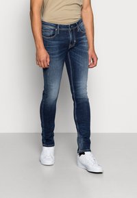 Smal passform, mörkblå denimjeans med en blekt ytstruktur, fem fickor och silverfärgad hårdvara. Matchas med vita sneakers.