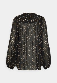 Blouse noire transparente à pois irréguliers beige, manches longues bouffantes et empiècement en yoke dans le dos.