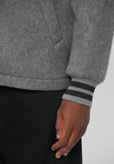 Γκρι φούτερ από πλέγμα με υφή, διαθέτει τσέπη καγκουρό. Οι μανσέτες έχουν μαύρες και γκρι ριγέ λεπτομέρειες.