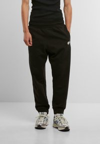 Svarta sweatpants med en avslappnad passform, med elastisk midja och sidofickor. Noterbar liten vit logotyp på vänster framsidan.