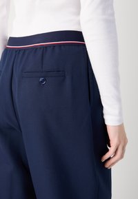 Pantaloni navy con una texture liscia, caratterizzati da una vita a righe in contrasto, tasca posteriore con dettaglio di bottone e vestibilità sartoriale.