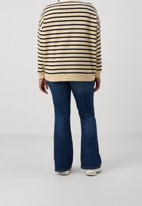 Su�éter beis con rayas horizontales negras, corte holgado, mangas largas. Combinado con jeans acampanados azules y zapatillas blancas. Vista trasera.