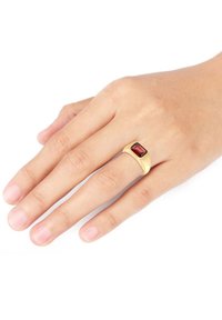 Goldring mit einem rechteckigen roten Stein, glatte Oberfläche, einfaches Banddesign, getragen an einer menschlichen Hand mit natürlicher Nagelfarbe.