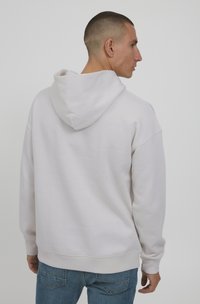 Hellgrauer Hoodie aus weichem Stoff, mit einer vollen Kapuze, gerippten Bündchen und Saum. Die Rückansicht zeigt eine entspannte Passform und ein einfaches Design.