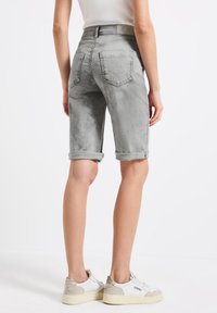 Bermudas de mezclilla gris con dobladillos enrollados, bolsillos traseros y una textura suave; combinadas con zapatillas blancas y beige.