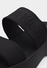 Μαύρο σανδάλι με δύο φαρδιές υφασμάτινες λουριά, το ένα με ανάγλυφο το όνομα της μάρκας "Bikkembergs", και χοντρή, υφασμένη σόλα.