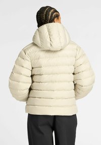 Chaqueta tipo plumón en beige claro, con capucha, diseño acolchado y puños elásticos. Textura suave con canalones horizontales.