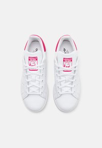 Vita lädersneakers med rosa accent vid hälen och tungan, med perforeringar och vita snören. Logotyp synlig på tungan.