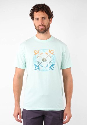 T-shirt en coton vert menthe clair comportant un design graphique circulaire avec des accents bleus, oranges et gris. Manches courtes, col rond.