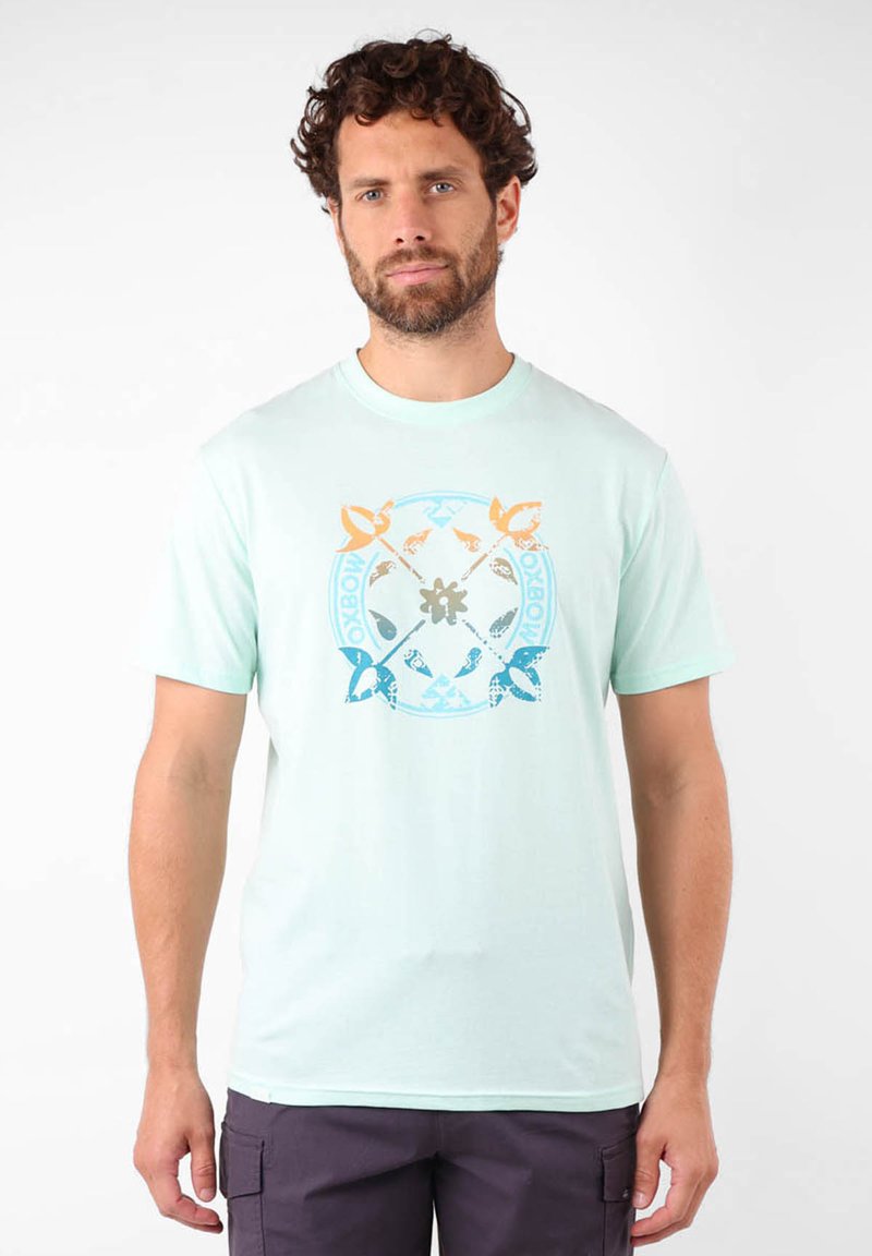 Camiseta de algodón en verde menta claro con un diseño gráfico circular que presenta acentos en azul, naranja y gris. Mangas cortas y estilo de cuello redondo.