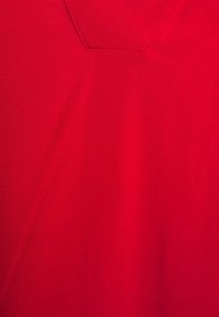 Red cotton fabric with a smooth texture, featuring a V-shaped neckline and minimal stitching details.