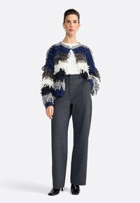 Suéter con flecos texturizados en tonos azul marino, gris y blanco; combinado con pantalones de talle alto grises y zapatos de tacón negros.