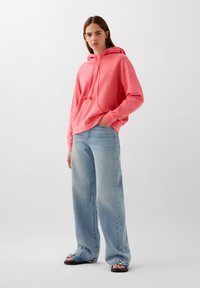 Roze hoodie met een trekkoord, gecombineerd met lichtblauwe wijde jeans en platte sandalen. Glad stof met een ontspannen pasvorm.