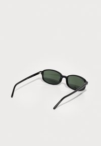 Gafas de sol negras con lentes verde oscuro, de forma ovalada, textura suave, con brazos negros elegantes y acentos de hardware mínimos.