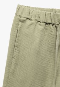 Pantalones de tela texturada de color verde claro con cintura elástica, detalle de cordón y bolsillos laterales. Diseño suave y casual para mayor comodidad.