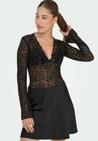 Svart lace långärmad topp med en scallopad halsringning, åtsittande liv och ett strukturerat blommönster, tillsammans med en slät svart kjol.
