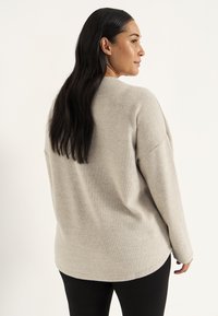 Beige geribde trui met een relaxte pasvorm, lange mouwen en een ronde zoom. De achterkant toont een gladde textuur en subtiele ontwerpelementen.