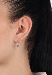 Silver hoopörhänge med sammanslingrat mönster, med en polerad yta och texturerade detaljer. Hänger från örsnibben.