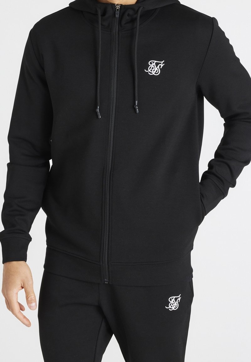 Sudadera con cremallera negra hecha de tejido suave, con cremallera frontal, capucha con cordón y pequeño logo blanco en el lado izquierdo del pecho.