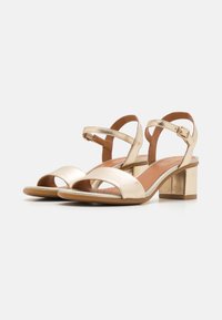 Gold strappy sandals with open toes, featuring a chunky heel and ankle buckle, smooth metallic finish, and cushioned footbed.