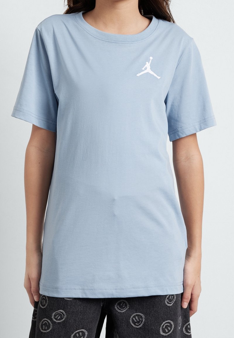 Svetle modré bavlněné tričko s krátkým rukávem, kulatým výstřihem a bílým vyšitým logem Jordan na levé straně hrudi. Hladká textura.