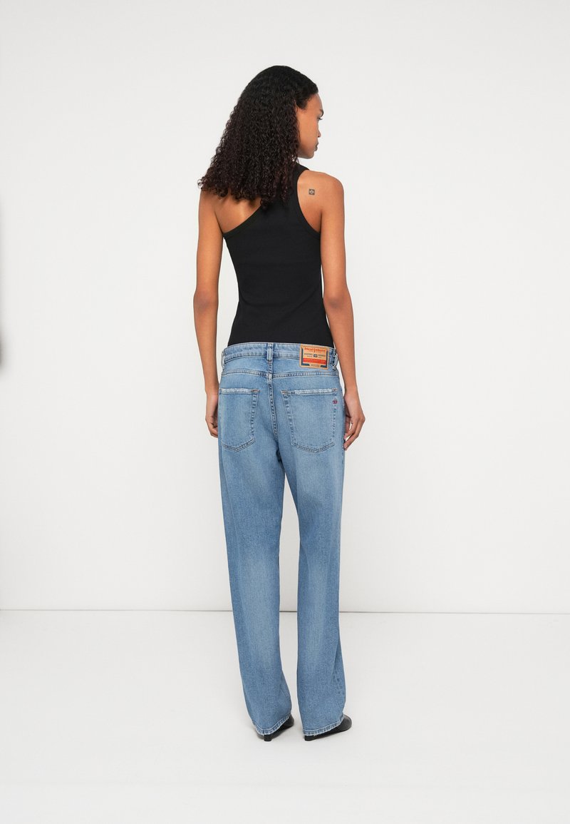 Blaue Jeans aus Denim mit einer lässigen Passform, hoher Taille und zwei Gesäßtaschen. Kombiniert mit einem figurbetonten schwarzen Tanktop.
