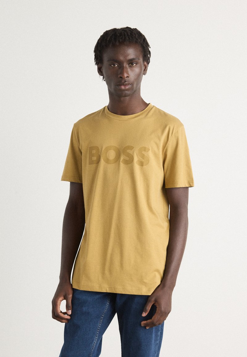 Short-sleeve mustard yellow T-shirt featuring a large, tonal "BOSS" logo on the front, made from soft cotton fabric.