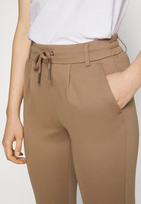 Bruine tapse broek met een trekkoordtaille en metalen accenten, voorzien van zijzakken en een gladde, gestructureerde stof.