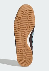 Rubber outsole with a grooved, textured pattern in light brown, featuring circular grips and a dark brown upper with blue accents.