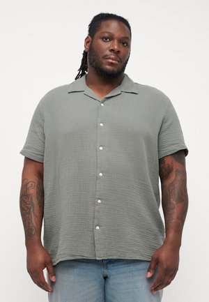 Short-sleeve button-up shirt in textured light green fabric with a spread collar and white buttons, paired with light blue jeans.