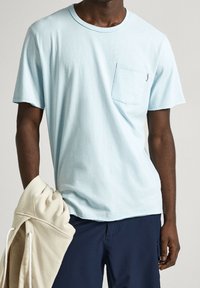 Lyseblå T-shirt med korte ærmer og brystlomme. Lavet af et blødt materiale med en glat tekstur. Bæreres med en cremet hættetrøje.