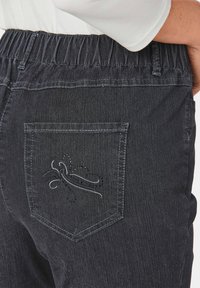 Pantalon en denim foncé avec une ceinture élastique, doté d'une poche arrière ornée d'un design brodé subtil et de strass.
