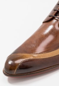 Chaussure en cuir marron avec une finition brillante, dotée d'un bout arrondi, d'une bande accentuée couleur beige et d'un design classique à lacets. Texture lisse et détails de couture.